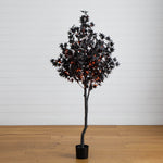A black artificial tree with star-shaped leaves and warm orange fairy lights, standing in a black pot on a light wood floor against a white paneled wall.