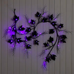 Black metal vine wall decor with glowing purple LED lights, mounted on a white paneled wall.