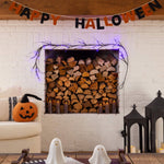 A cozy Halloween-themed living room scene featuring a built-in wood fire with purple string lights, a 'HAPPY HALLOWEEN' banner, a white brick wall, a pumpkin on a sofa, and ghost decorations in the foreground.