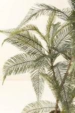 Close-up of artificial palm fronds with fine, feathery green leaves on a light cream background.