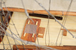 Model ship with a grater on the deck, viewed through chain-link fence.