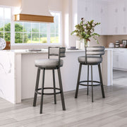 Two gray cushioned bar stools in a kitchen setting with white cabinets and a window view.