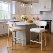 Modern kitchen with white island and bar stools, featuring a vase of flowers and fruit bowl.