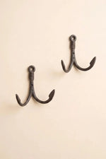 Two black metal fishing hook wall hooks mounted on a plain beige wall.