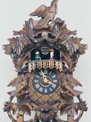 Wooden cuckoo clock with intricate carvings and two figures inside on a white background