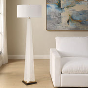 White floor lamp in a living room with a white sofa and abstract painting on the wall.