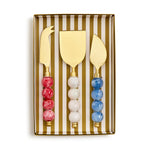 Set of three gold cheese knives with colorful bead handles in a striped box