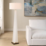 White floor lamp in a living room with a white sofa and abstract painting on the wall.