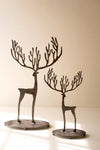Two metal deer figurines with antlers, one large and one small, both standing on oval bases against a warm beige background.