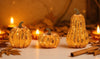 Decorative pumpkins with string lights on a table with candles and cinnamon sticks.