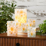 Set of floral-patterned candles on a wooden surface with plants in the background