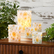 Set of floral-patterned candles on a wooden surface with plants in the background