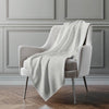 Light gray textured blanket draped over a gray armchair against a gray paneled wall.