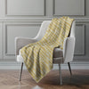 Yellow patterned blanket draped over a gray armchair against a gray wall.