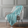 Turquoise blanket with white patterns draped over a gray chair against a gray wall.