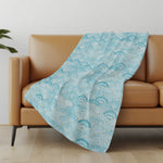 Turquoise patterned blanket draped over a brown sofa in a room with a light-colored wall and wooden floor.