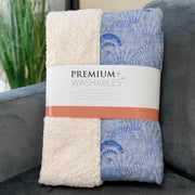 Two folded blankets, one white and one with blue shell pattern, on a couch with 'Premium Washables' packaging.