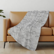 Gray patterned blanket draped over a brown sofa in a room with a light-colored wall and wooden floor.