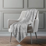 Gray patterned blanket draped over a white armchair against a gray paneled wall.