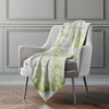 White chair with a green and white patterned blanket draped over it against a gray wall.