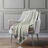 Light green blanket with shell pattern draped over a gray armchair against a gray wall.