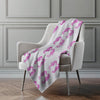 White chair with a pink seahorse patterned blanket draped over it against a gray wall.