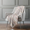 Light gray armchair with a patterned blanket draped over it against a neutral wall.