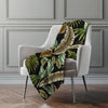 Tropical leaf patterned blanket draped over a chair in a room with gray walls.