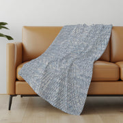Blue patterned throw blanket draped over a brown sofa in a living room setting.