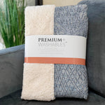 Two folded blankets, one white and one gray with a pattern, on a couch with 'Premium Washables' packaging.