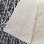 Close-up of a textured white rug with a contrasting patterned rug underneath.