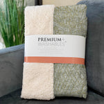 Two folded blankets, one white and one patterned green, with a 'Premium Washables' label on a gray surface.