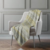 Gray armchair with a green and yellow plaid blanket draped over it against a gray wall.