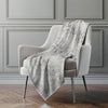 Gray patterned blanket draped over a gray armchair against a gray wall.