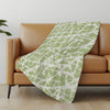 Green and white patterned blanket draped over a brown sofa in a room with a light gray wall.