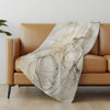 Beige marble-patterned throw blanket draped over a brown sofa in a room with a light-colored floor and wall.