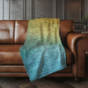 Gradient green and blue blanket draped over a brown leather sofa in a room with dark paneled walls.