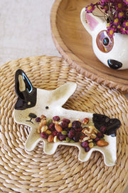 Dog-shaped ceramic dish filled with dried fruits on a woven mat