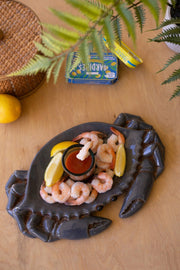 Crab-shaped platter with shrimp and lemon wedges on a wooden surface.