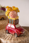 Red car-shaped vase with floral arrangement on a woven surface