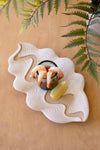 Decorative ceramic plate with shrimp and a small bowl on a wooden surface with fern leaves in the background.