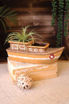 Wooden boat-shaped planter with a plant on a textured surface