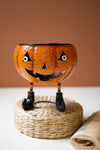 Halloween-themed decorative bowl with a face on a woven stand against a brown background