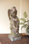 Stone angel statue on a wooden surface with plants in the background