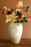 Decorative vase with floral arrangement on a wooden surface against a beige wall