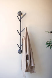 Black tree-shaped coat rack with a beige jacket on a white wall
