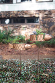 Two gold fish-shaped planters with honeycomb designs on stakes in a garden setting.