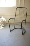 Wire mesh chair in a minimalistic room with a textured floor and light-colored walls.