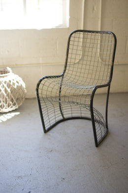 Wire mesh chair in a minimalistic room with a textured floor and light-colored walls.