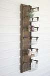 Wooden wall-mounted rack with metal baskets holding various items against a white wooden panel background.
